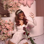 A woman wearing Ivory Sheep's Eloise Mini Lace Dress, surrounded by pink flowers.