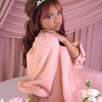 A woman in a peach tulle mini dress with a tiara against a pink draped background