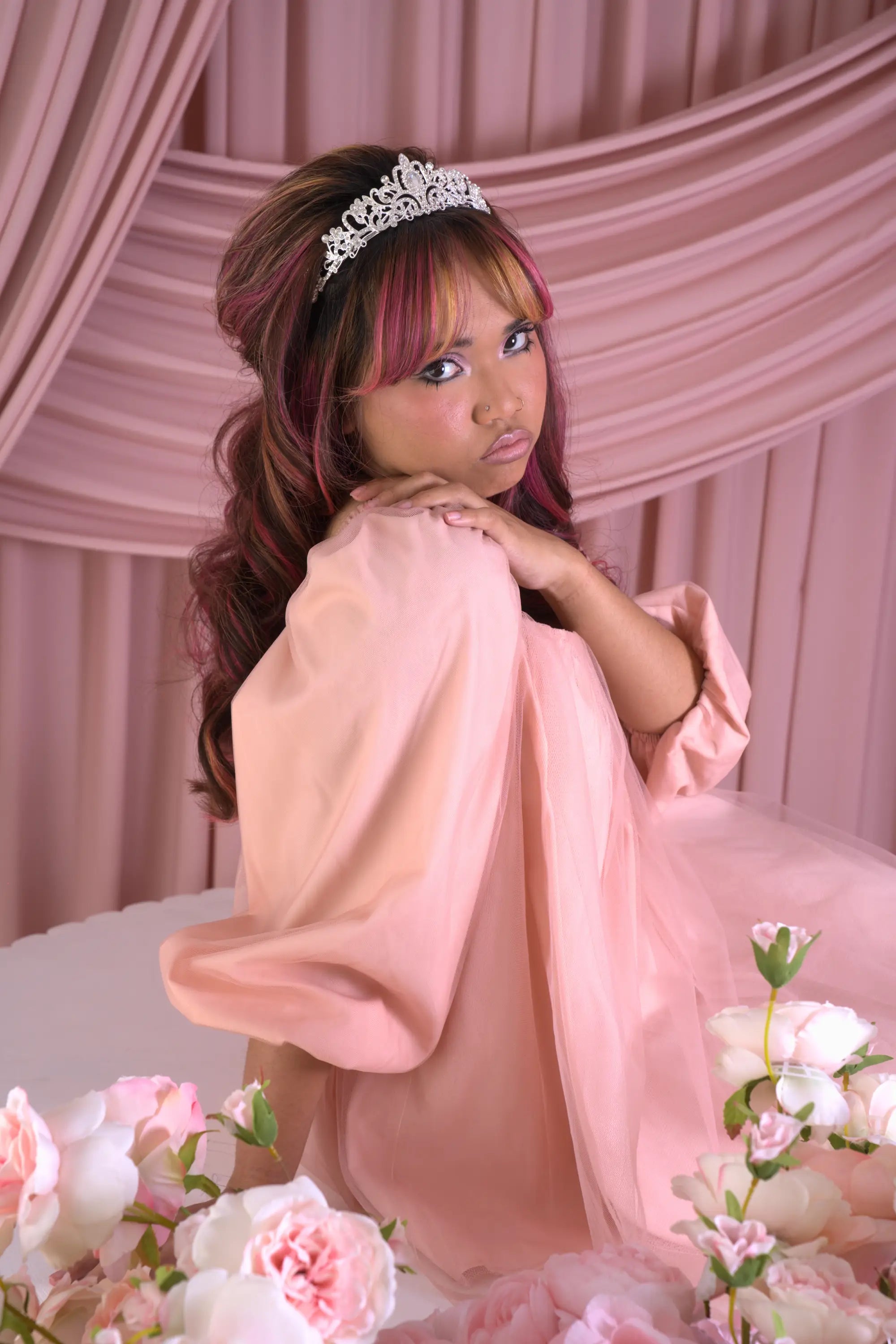 A woman in a peach tulle mini dress with a tiara against a pink draped background