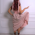 A woman wearing a pink floral dress with a hood against a white paneled wall.