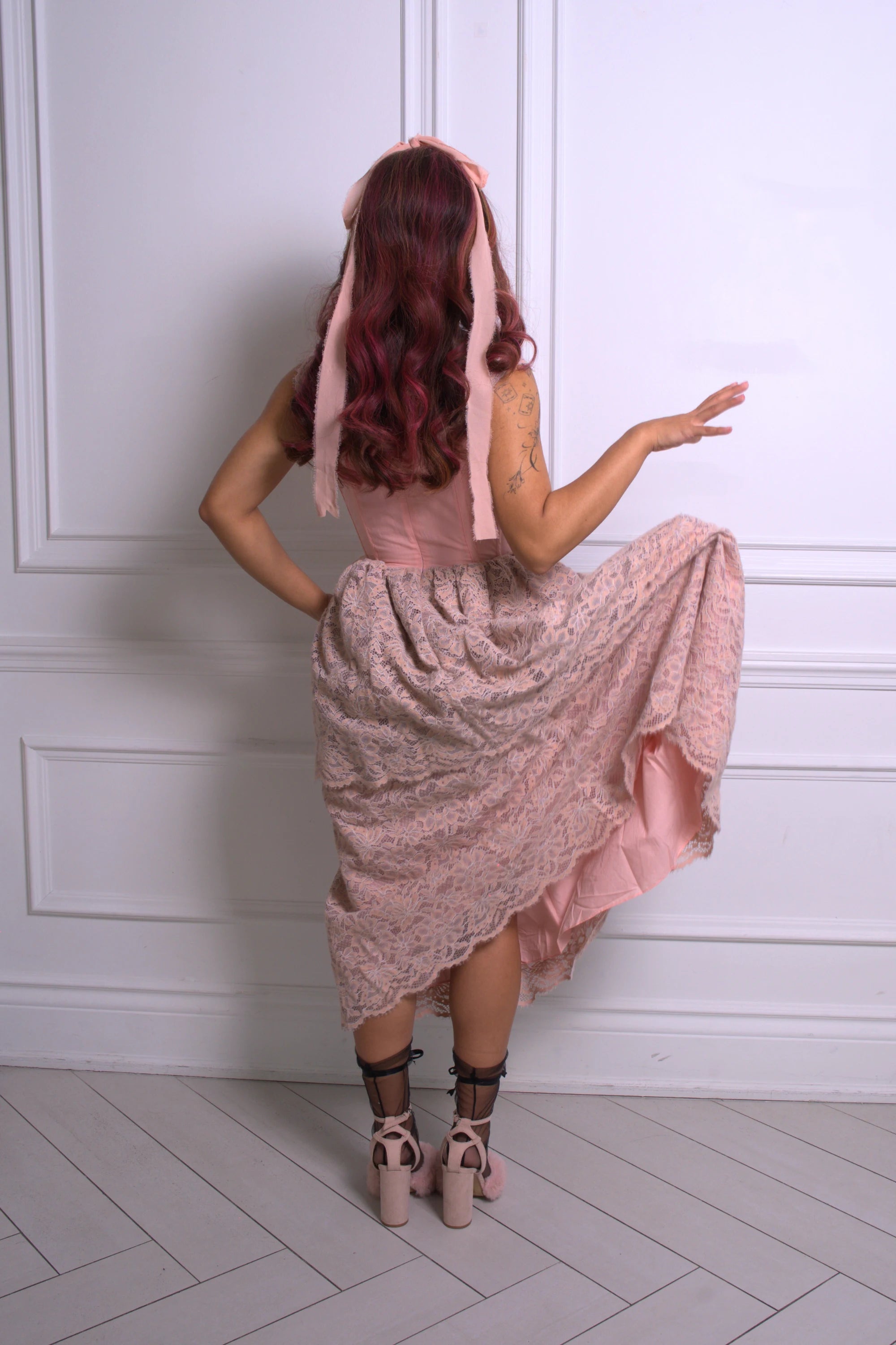 A woman wearing a pink floral dress with a hood against a white paneled wall.