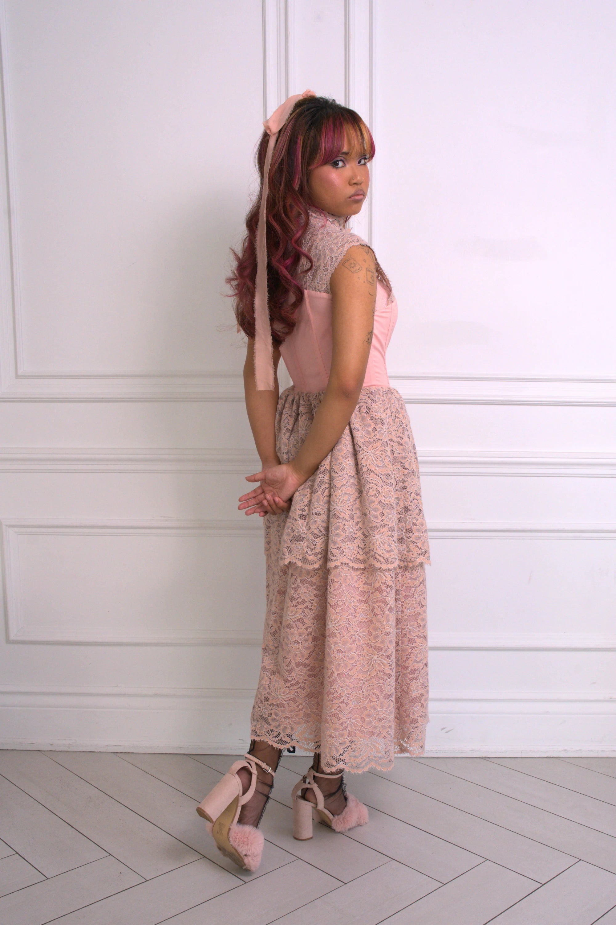 A woman wearing Ivory Sheep's Garden Party Lace Midi Dress against a white paneled wall.