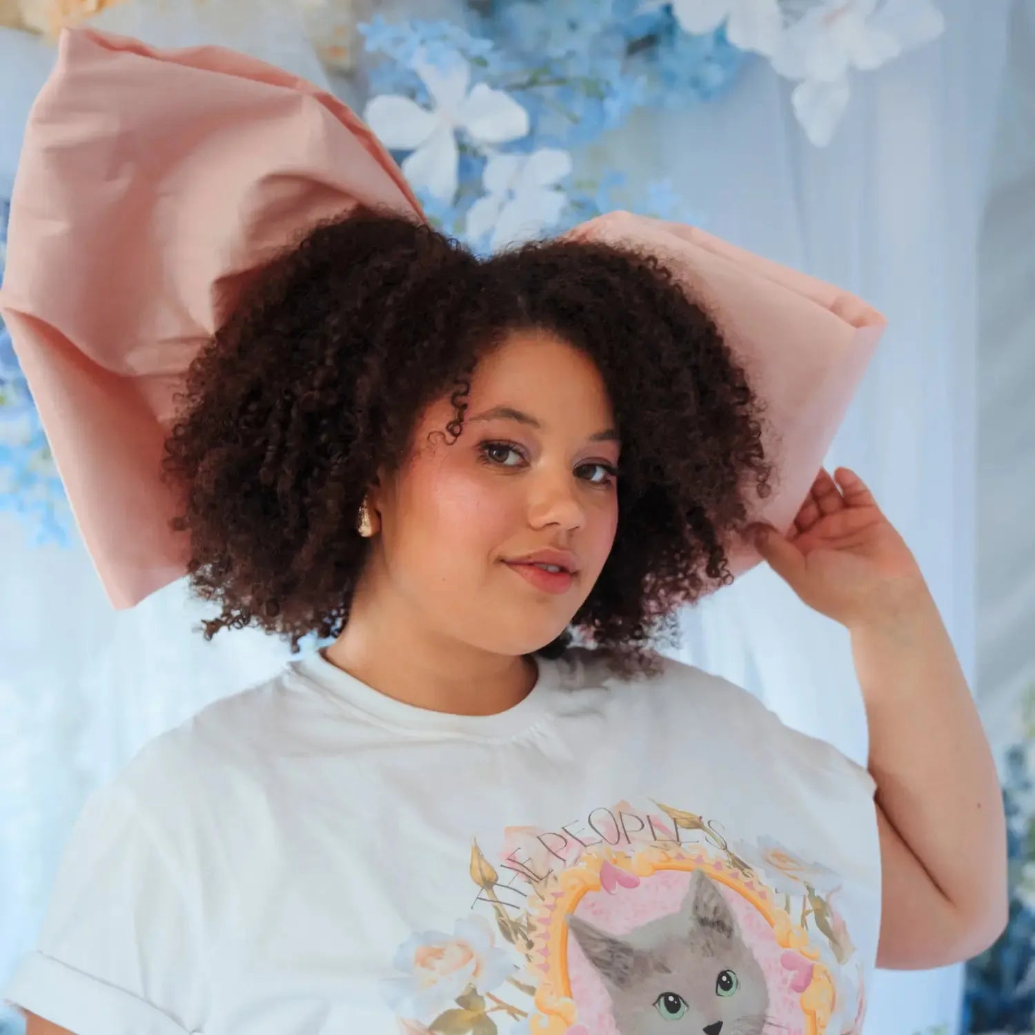 A woman wearing a giant pink hair bow against a floral, light blue background.