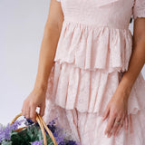 A woman wearing Ivory Sheep's Leighton Pink Cotton Mini Dress holding a basket of flowers against a white background.