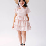A woman wearing a pink cotton dress with a straw hat on a white background.