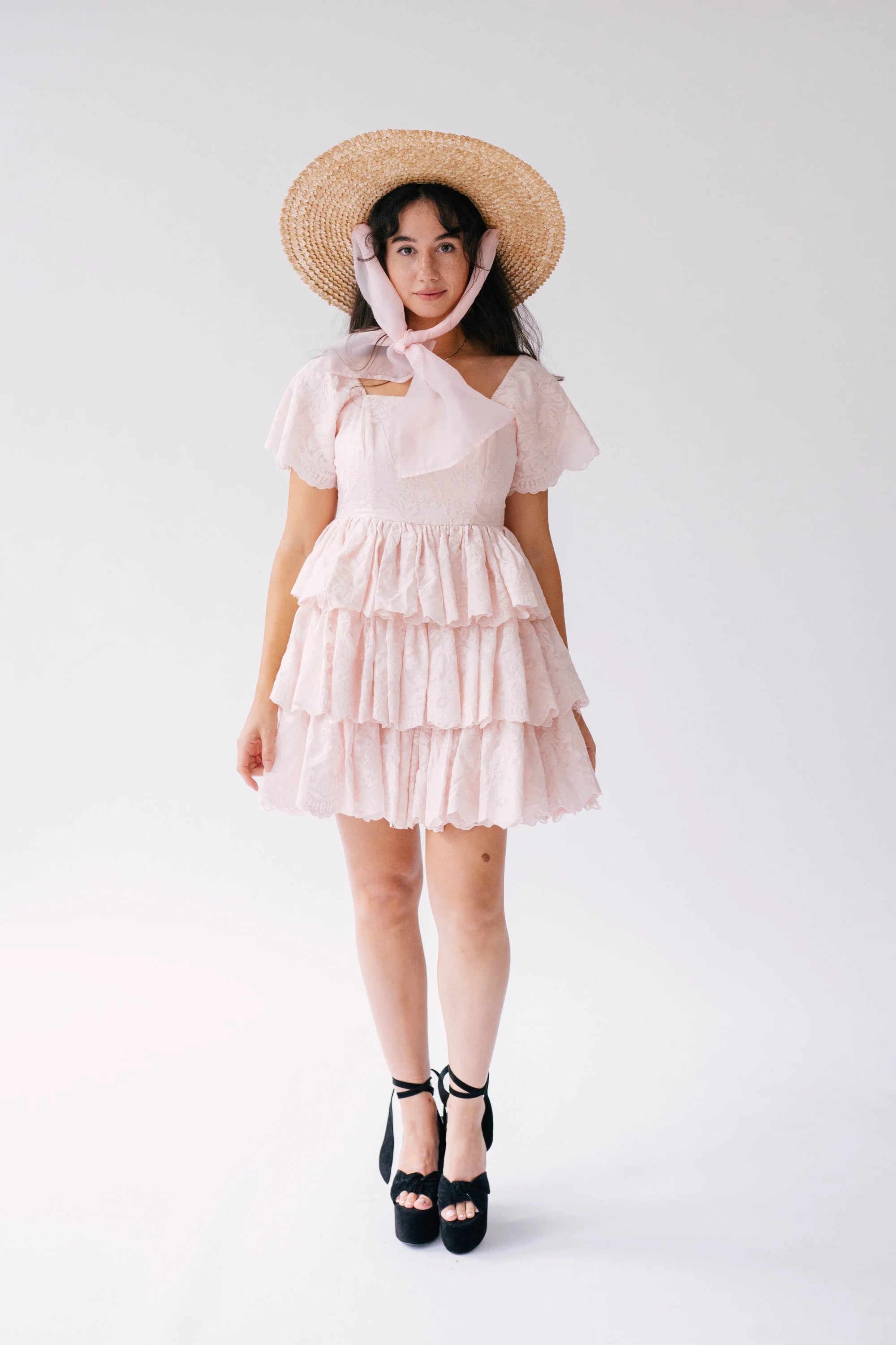 A woman wearing a pink cotton dress with a straw hat on a white background.
