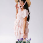 A woman wearing Ivory Sheep's Leighton Pink Cotton Mini Dress and straw hat holding a basket of flowers against a white background