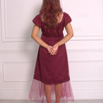 A woman wearing Ivory Sheep's crimson red Molly Midi Dress with a white paneled wall background