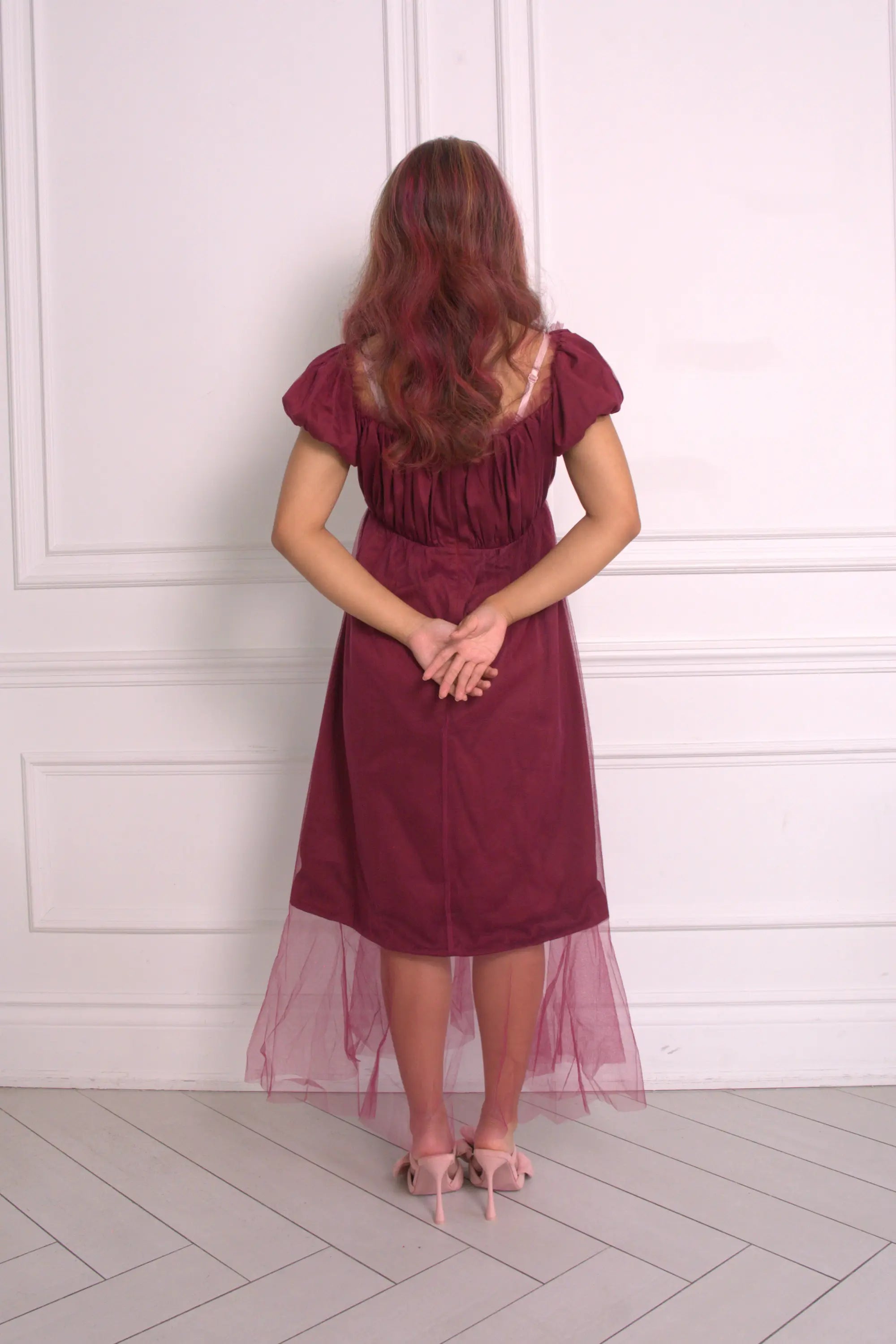 A woman wearing Ivory Sheep's crimson red Molly Midi Dress with a white paneled wall background