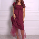 A woman wearing Ivory Sheep's crimson red Molly Midi Dress with a sheer overlay against a white paneled wall.