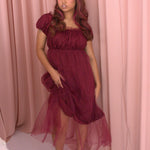 A woman wearing Ivory Sheep's crimson red Molly Midi Dress leaning against a pink curtain background