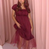 A woman wearing Ivory Sheep's crimson red Molly Midi Dress leaning against a pink curtain background