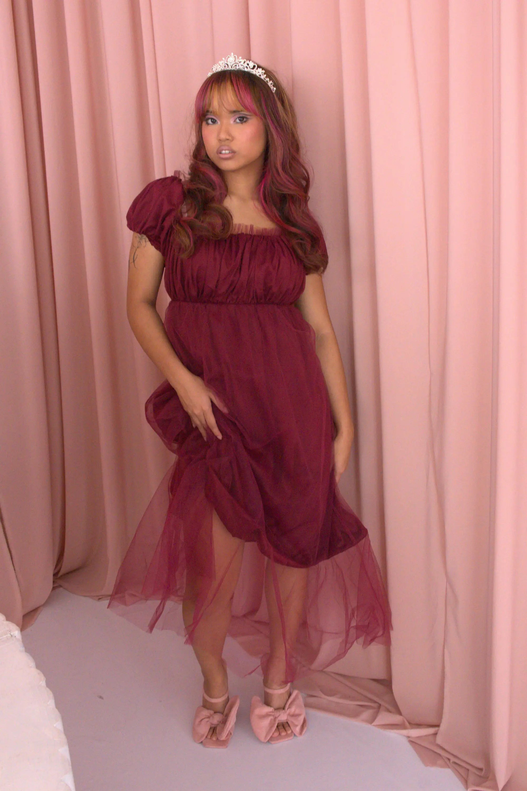 A woman wearing Ivory Sheep's crimson red Molly Midi Dress leaning against a pink curtain background