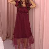 A woman wearing Ivory Sheep's crimson red Molly Midi Dress with a sheer overlay against a pink curtain background