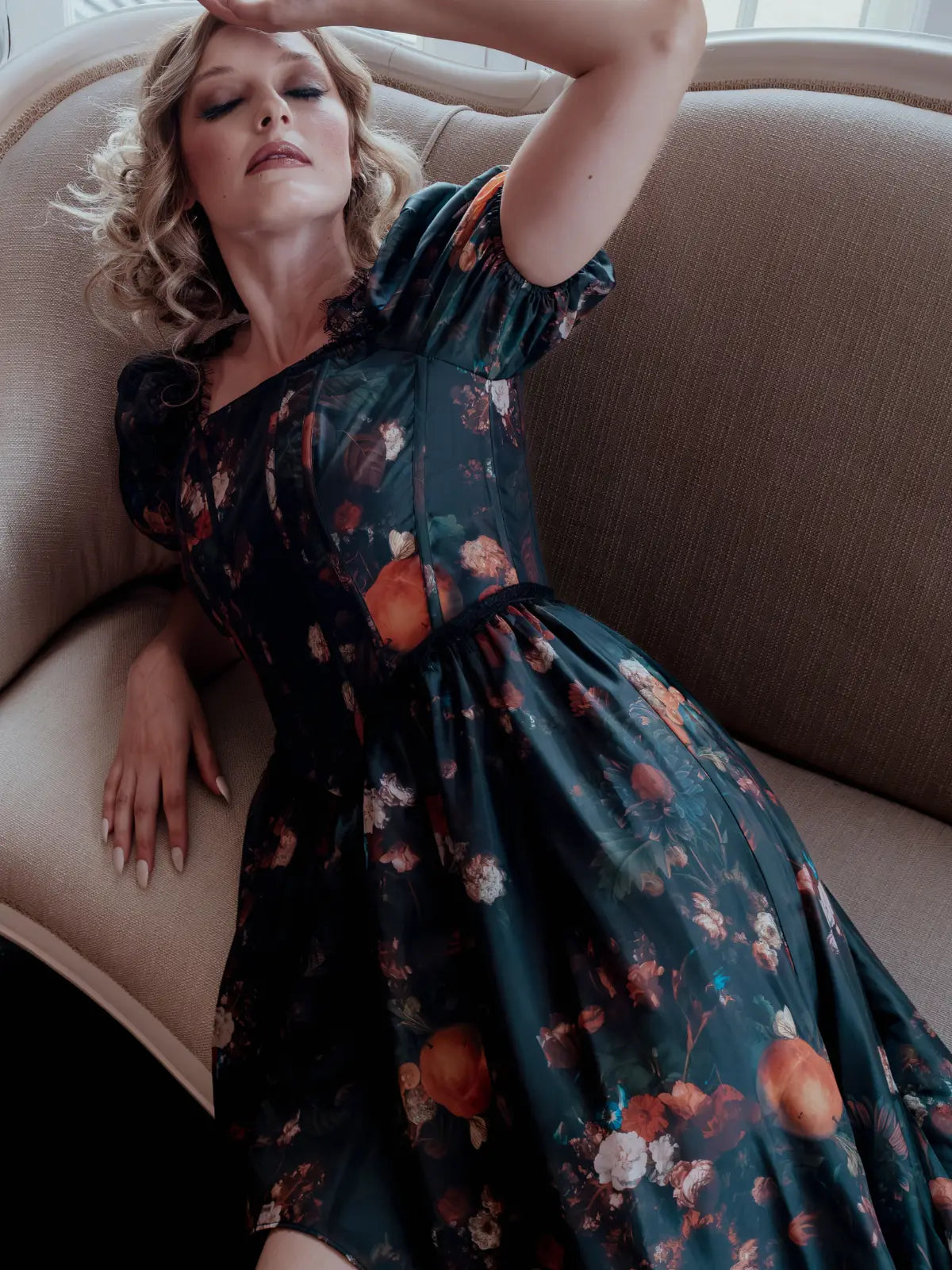 A woman in Ivory Sheep's Still Life Charlotte taffeta dress, lying on a beige couch