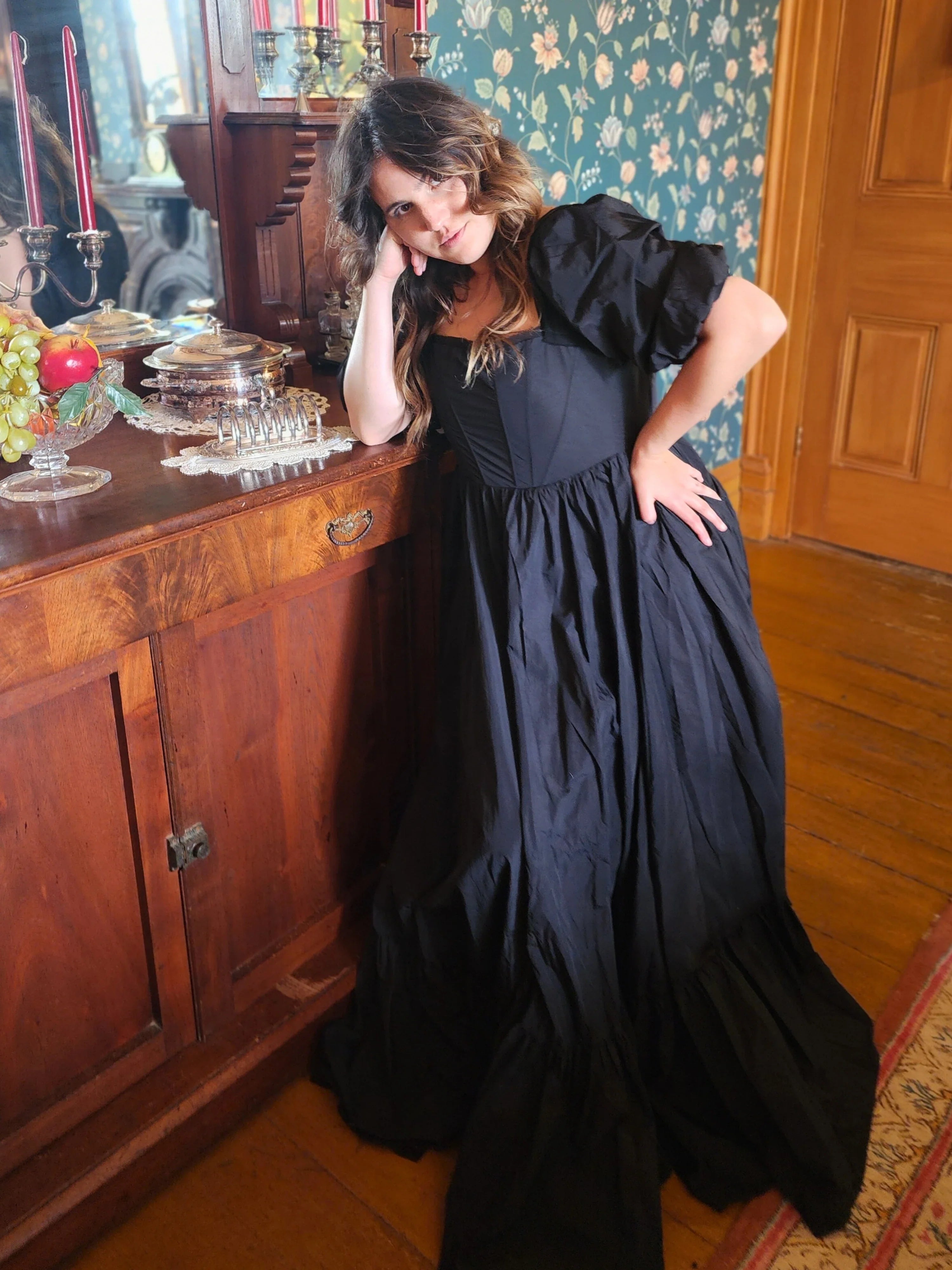 Woman in The Josephine Gown with classic puff sleeves leaning against wooden cabinet