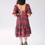 A back view of a woman wearing the Josephine tartan plaid dress, showcasing the tie-up corset bodice and midi length.