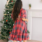 A back view of a woman wearing the Josephine tartan plaid dress with a decorated Christmas tree in the background.