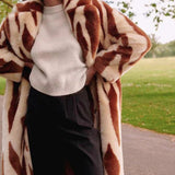 Katie Faux Fur Chestnut Tiger Duster Coat over sweater and dark pants with abstract shapes