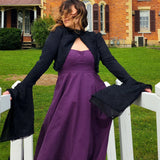 Woman in a purple dress and Lady Elizabeth jacket by a white fence