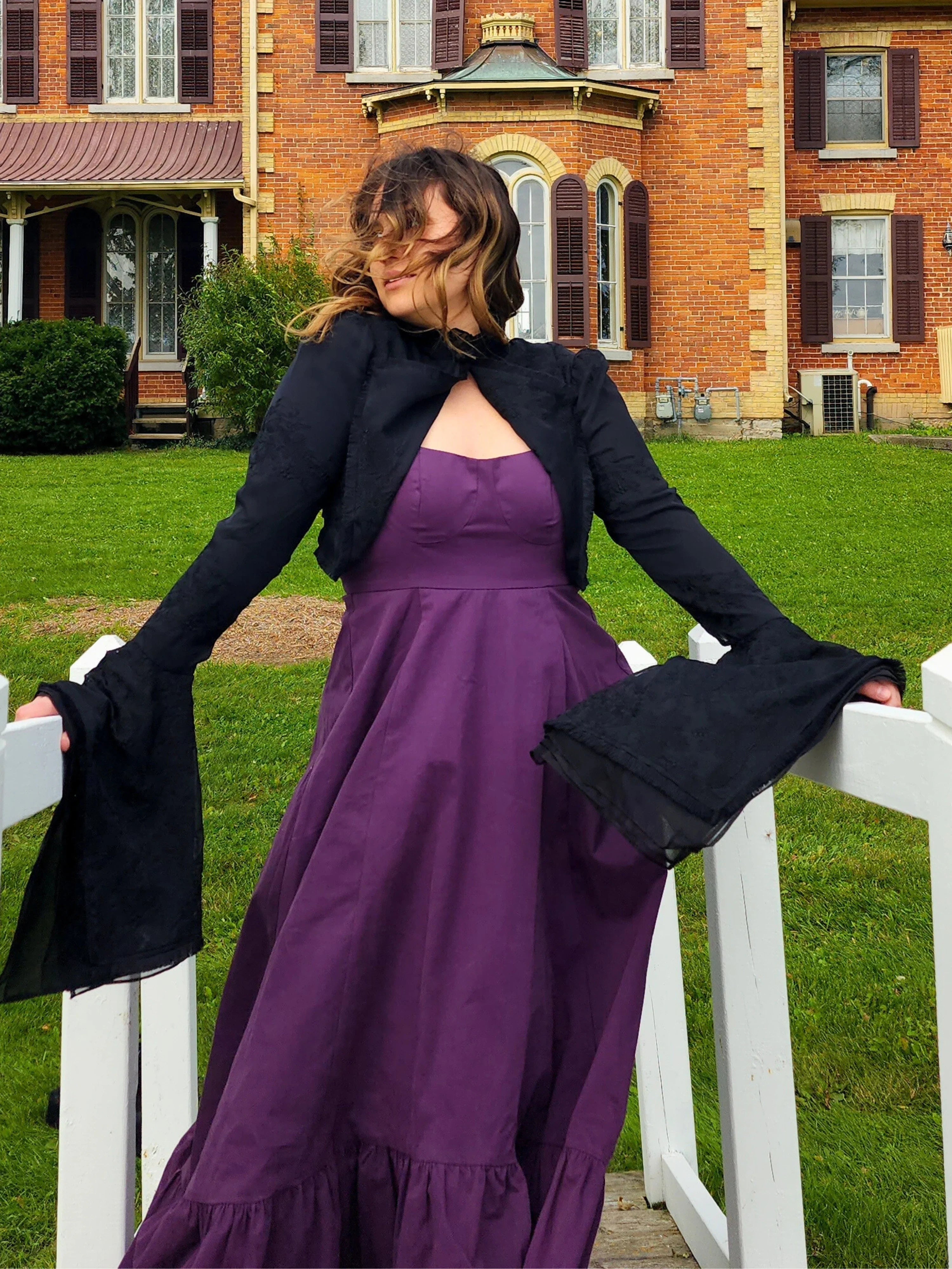 Woman in a purple dress and Lady Elizabeth jacket by a white fence