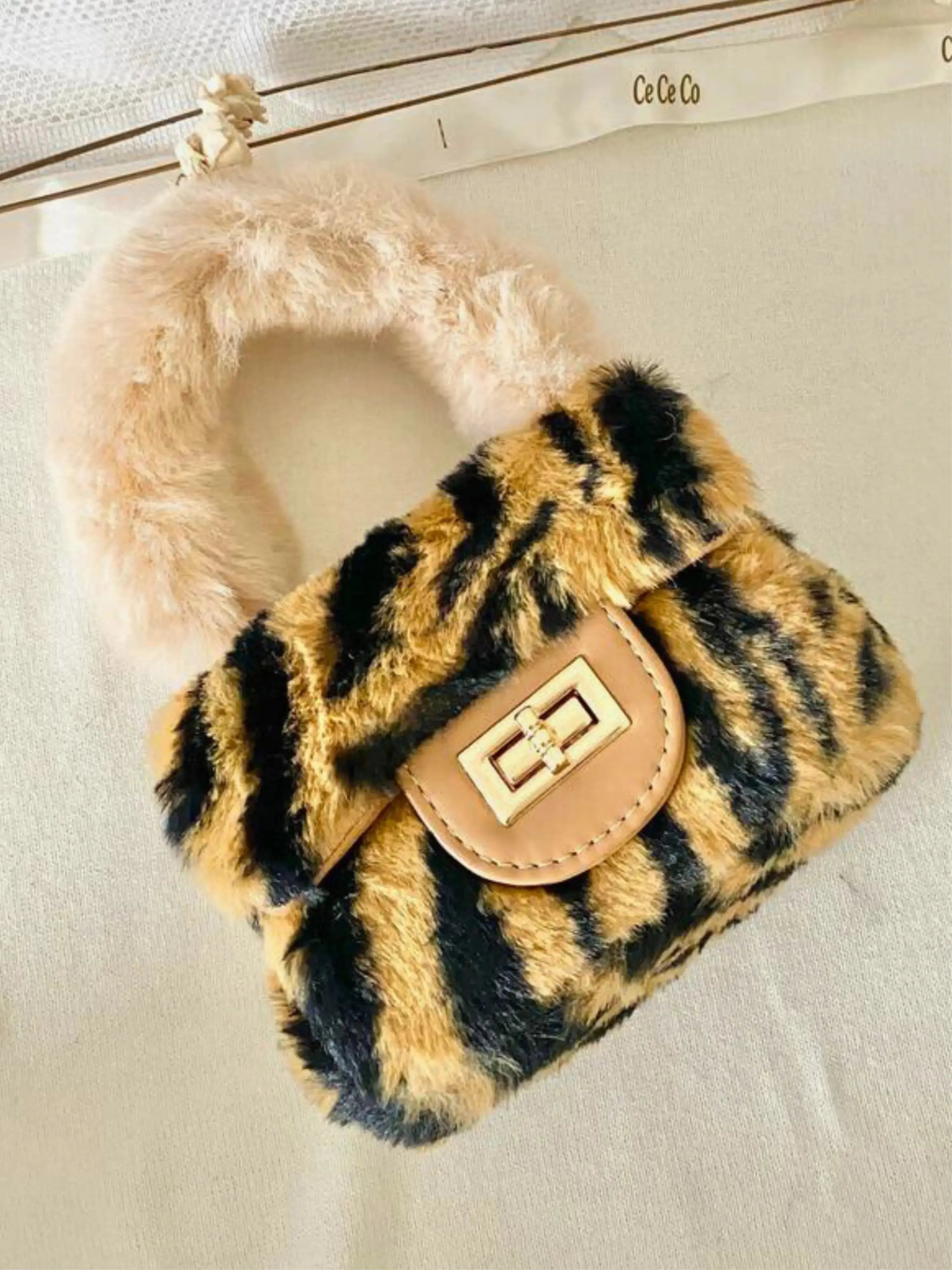 The Leopard Faux Fur Micro Purse features a bold leopard print design with a plush faux fur handle. It's shown on a plain table.
