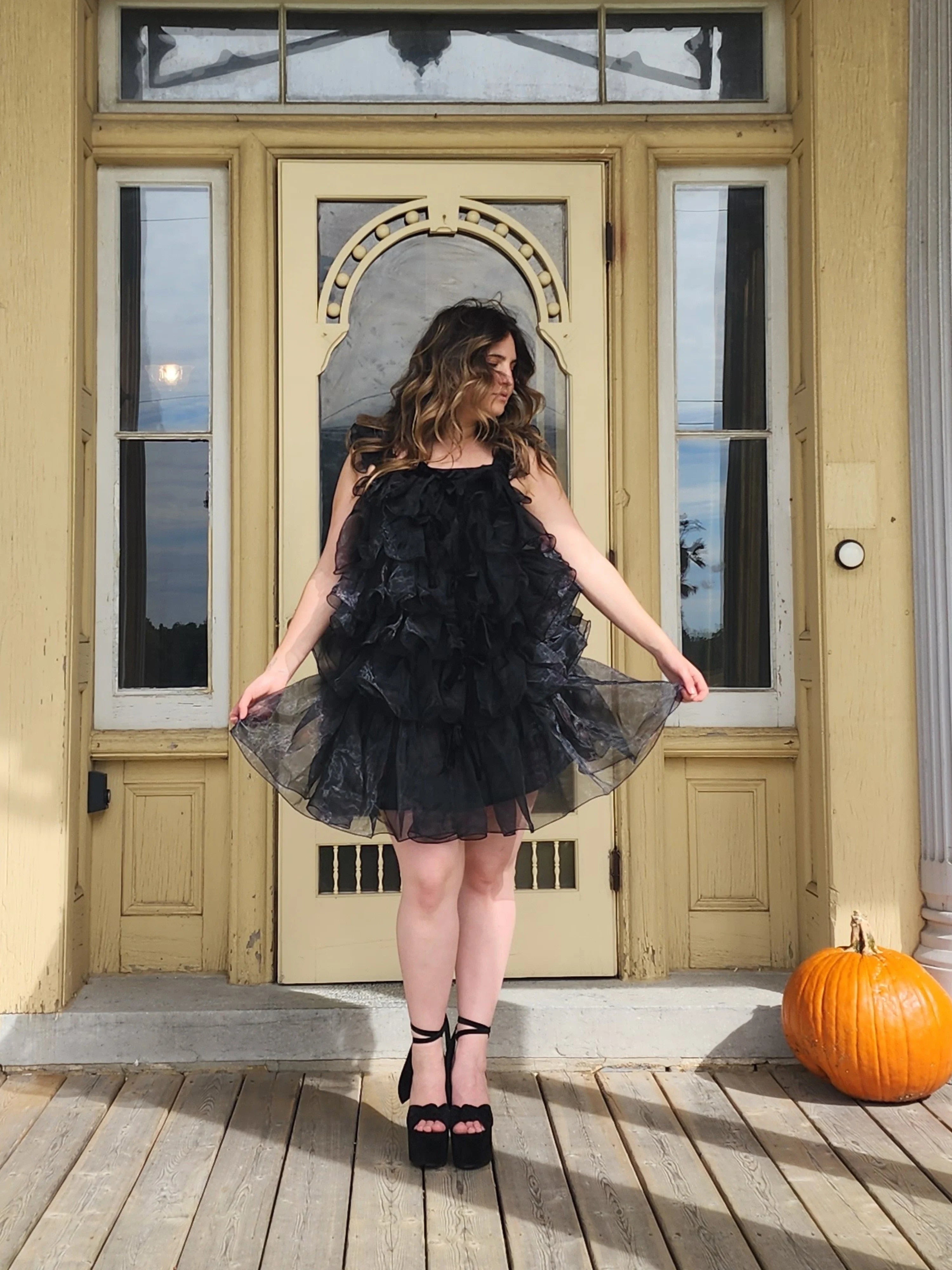 Woman in a frilly black feather mini dress standing elegantly in a doorway