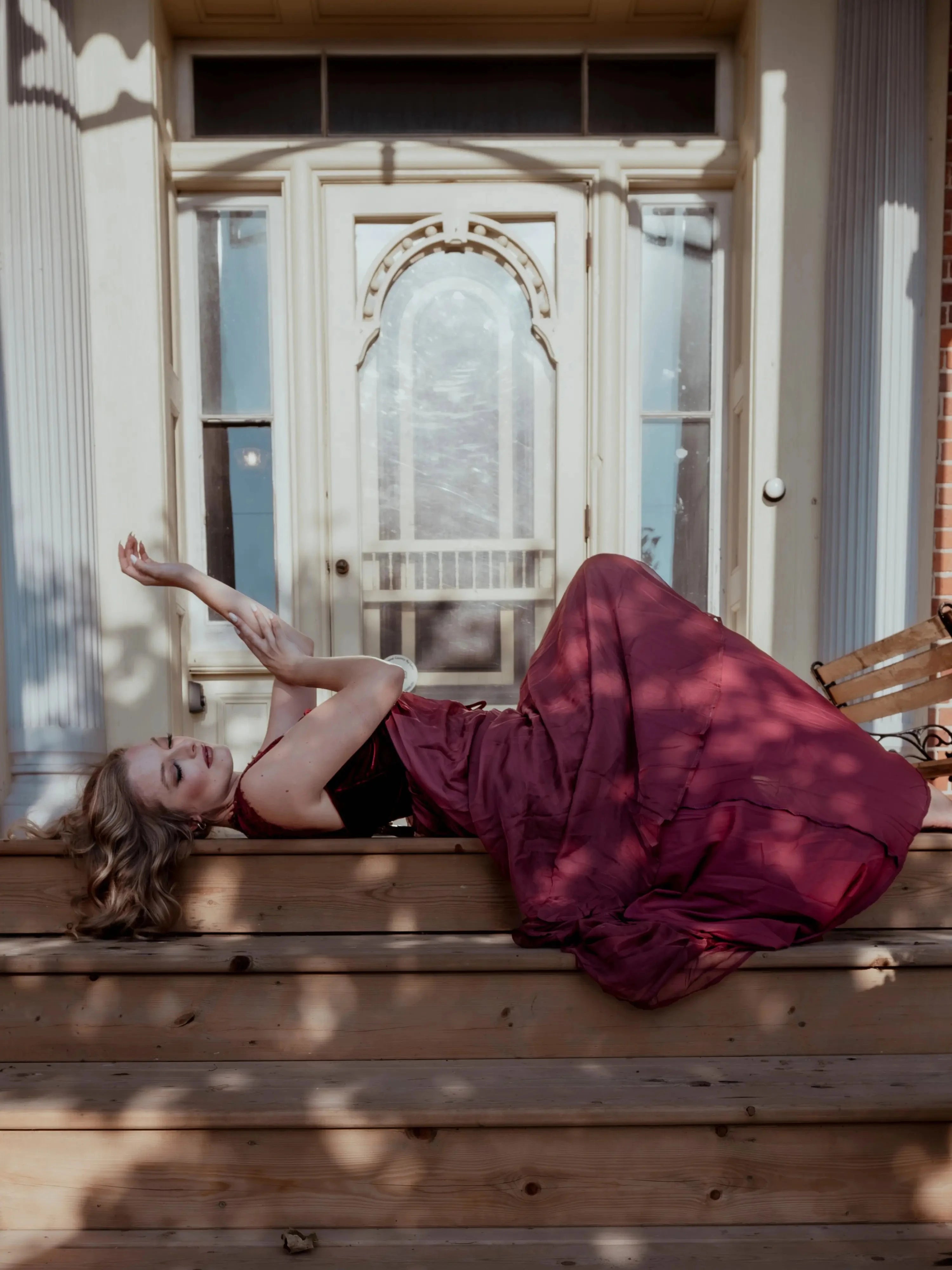 The Scarlet Red Scorned Lovers Gown styled outdoors, featuring a flowing red chiffon skirt and corset bodice, evoking Victorian romance.