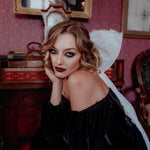A woman wearing the Nocturne Velvet Mini Dress with a white lace hair bow in a vintage room.
