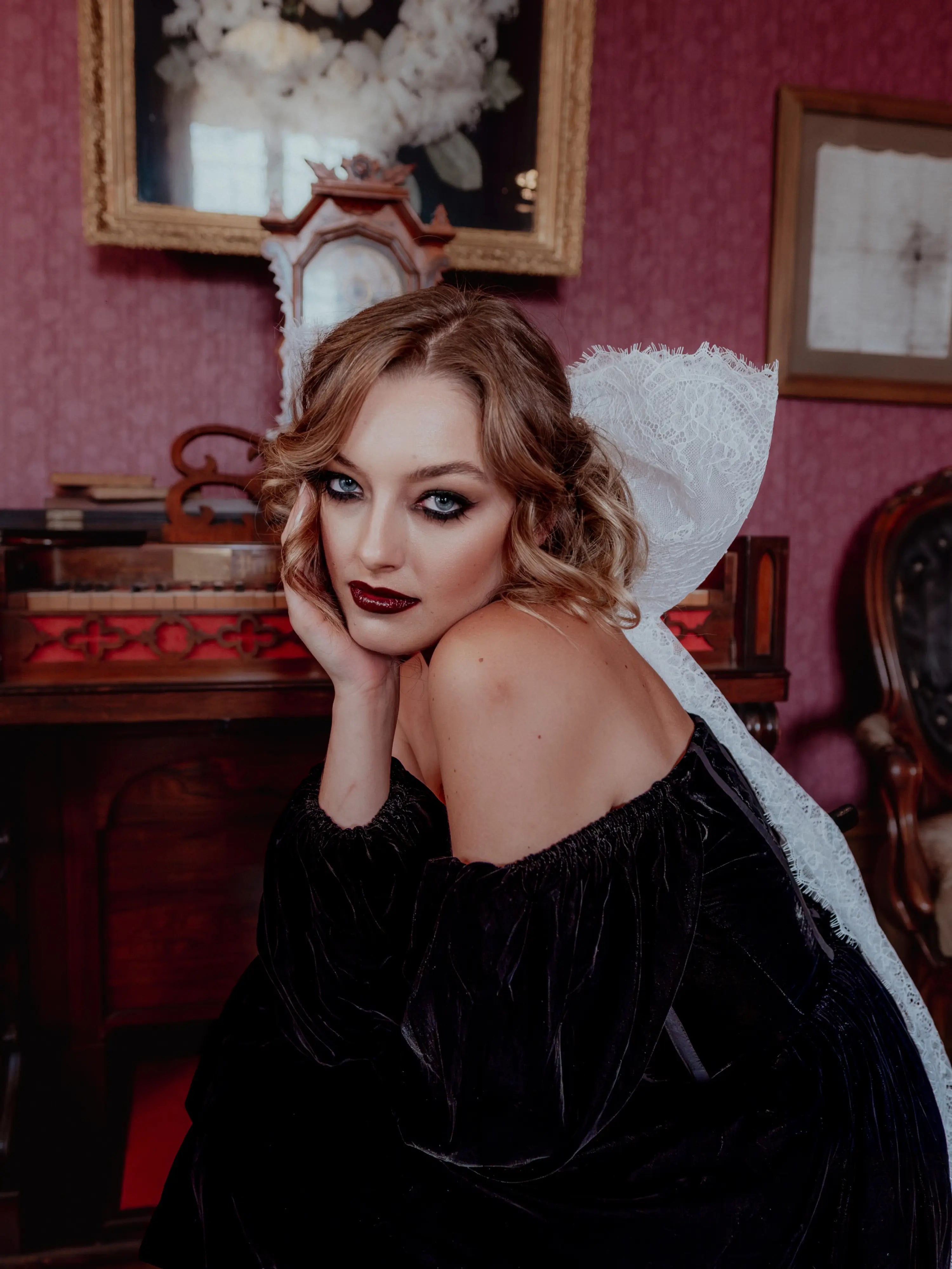 A woman wearing the Nocturne Velvet Mini Dress with a white lace hair bow in a vintage room.