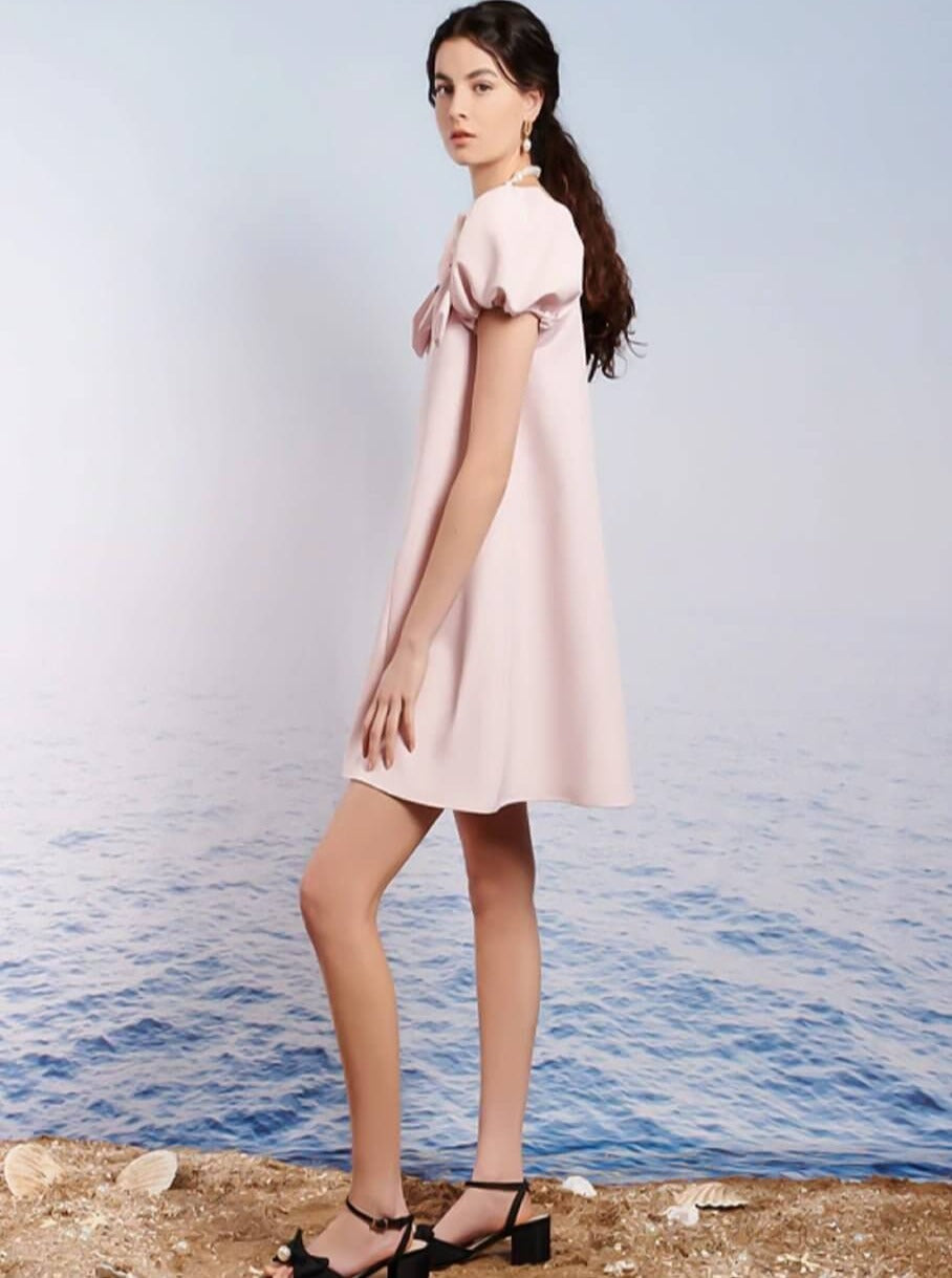 Pale pink Paddle Bow Mini Dress with puffed shoulders worn by a stylish woman