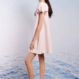 Pale pink Paddle Bow Mini Dress with puffed shoulders worn by a stylish woman