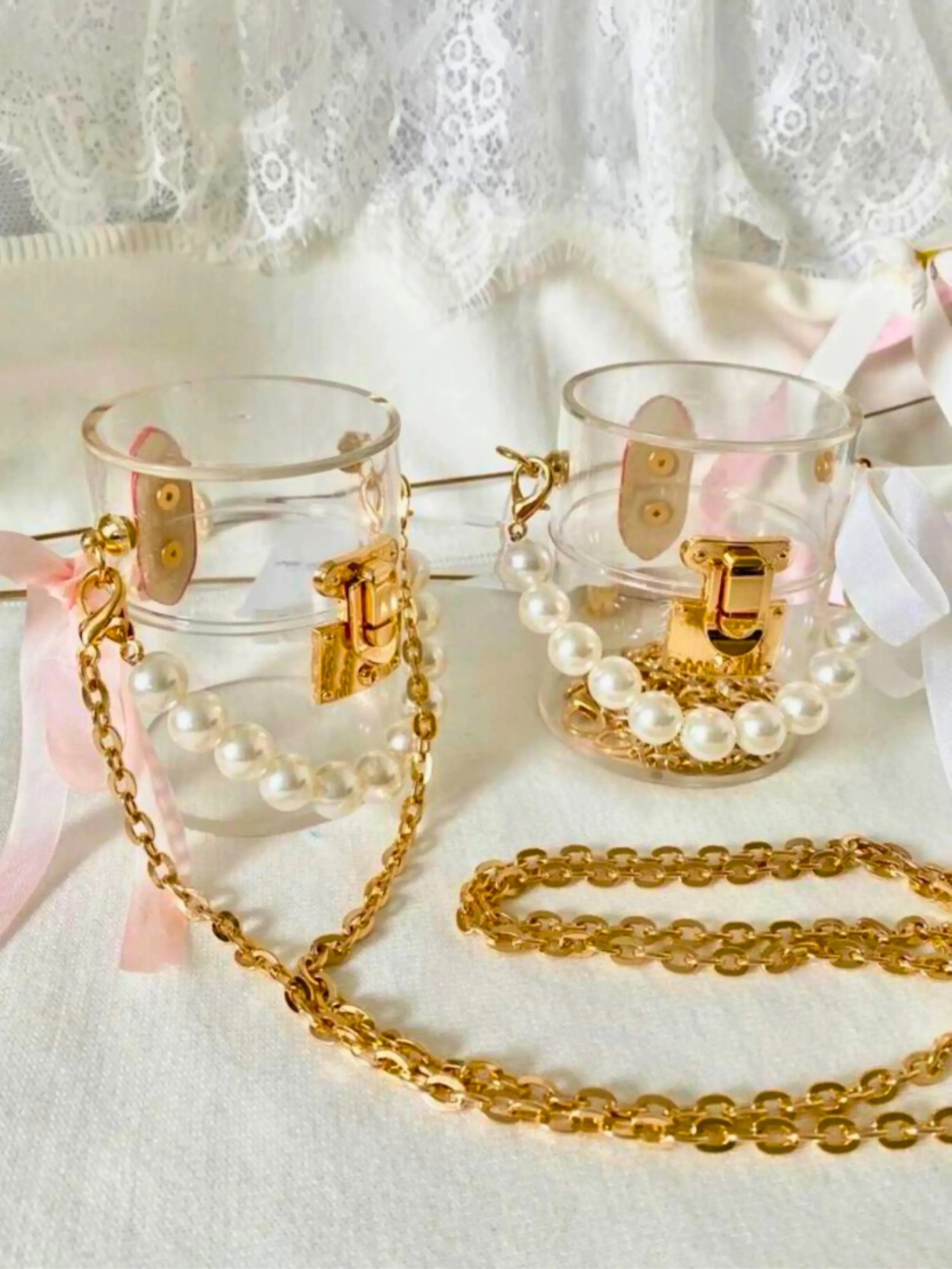 Clear mini bucket bags with gold chains and pearl accents on a white lace background