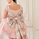 A woman wearing a pink cotton mini dress with an oversized grand bow.