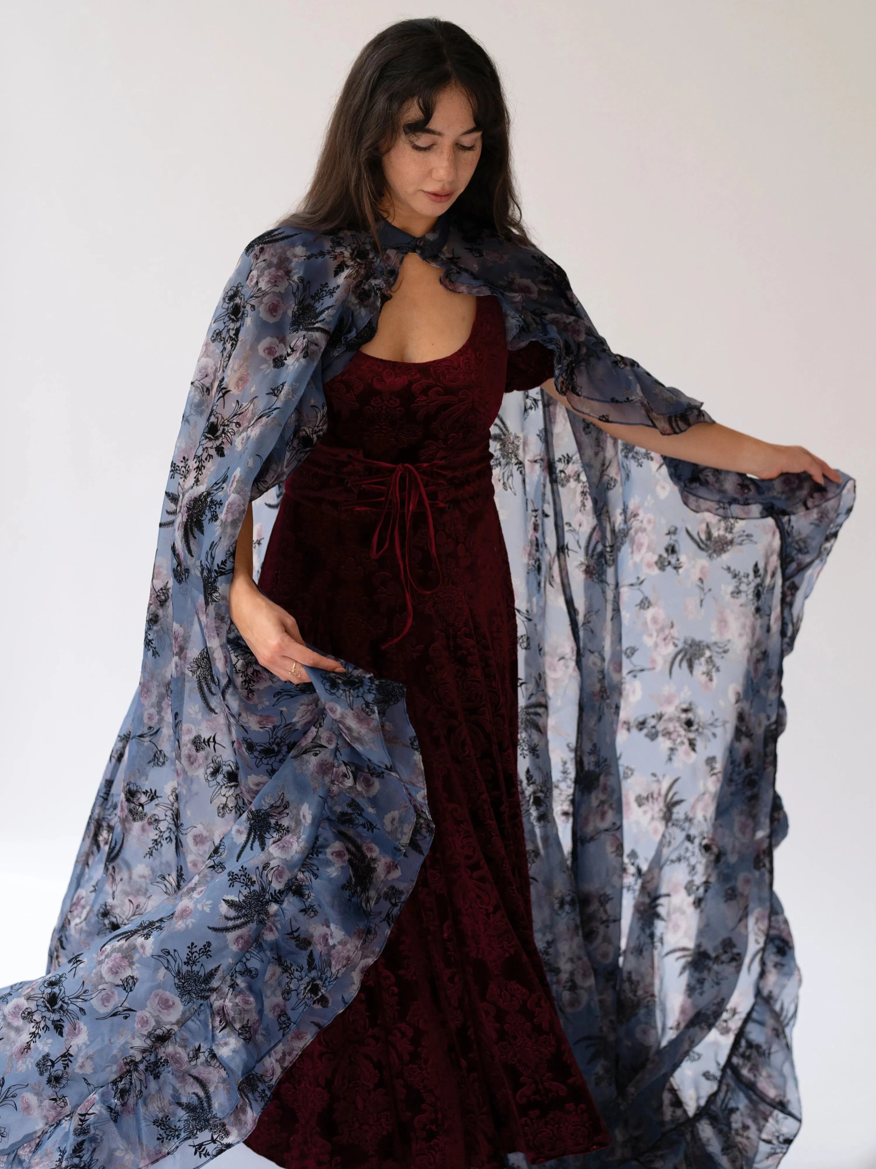 The High Priestess Victorian Cloak draped over a red dress, highlighting the sheer purple floral fabric and elegant Victorian silhouette.