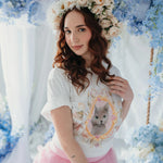 A woman wearing the Princess Kitten Tee styled with a floral crown and pink ruffled skirt, featuring whimsical cat artwork by Kaeti MacNeil.