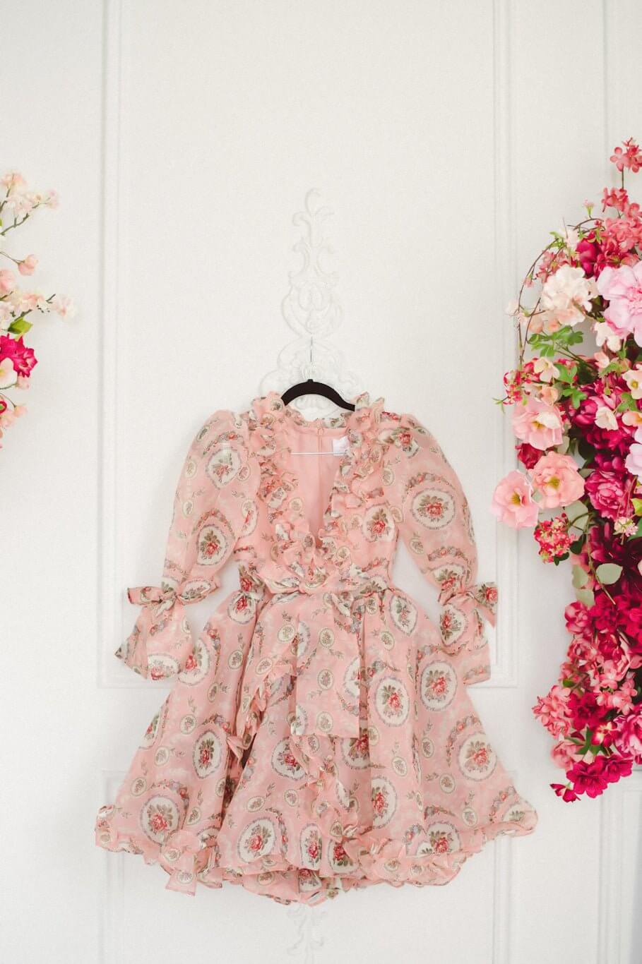 Pink floral Rapunzel Organza Marie Dress with long sleeves hanging on a wall