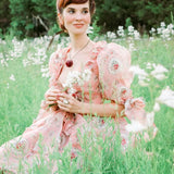 Woman in a pink floral dress in a field showcasing the Rapunzel Organza Marie Dress