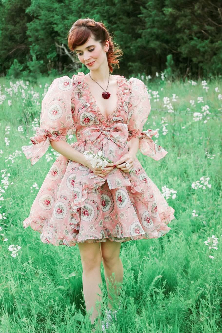 Woman in a pink floral Rapunzel Organza Marie Dress with puffy sleeves in a meadow