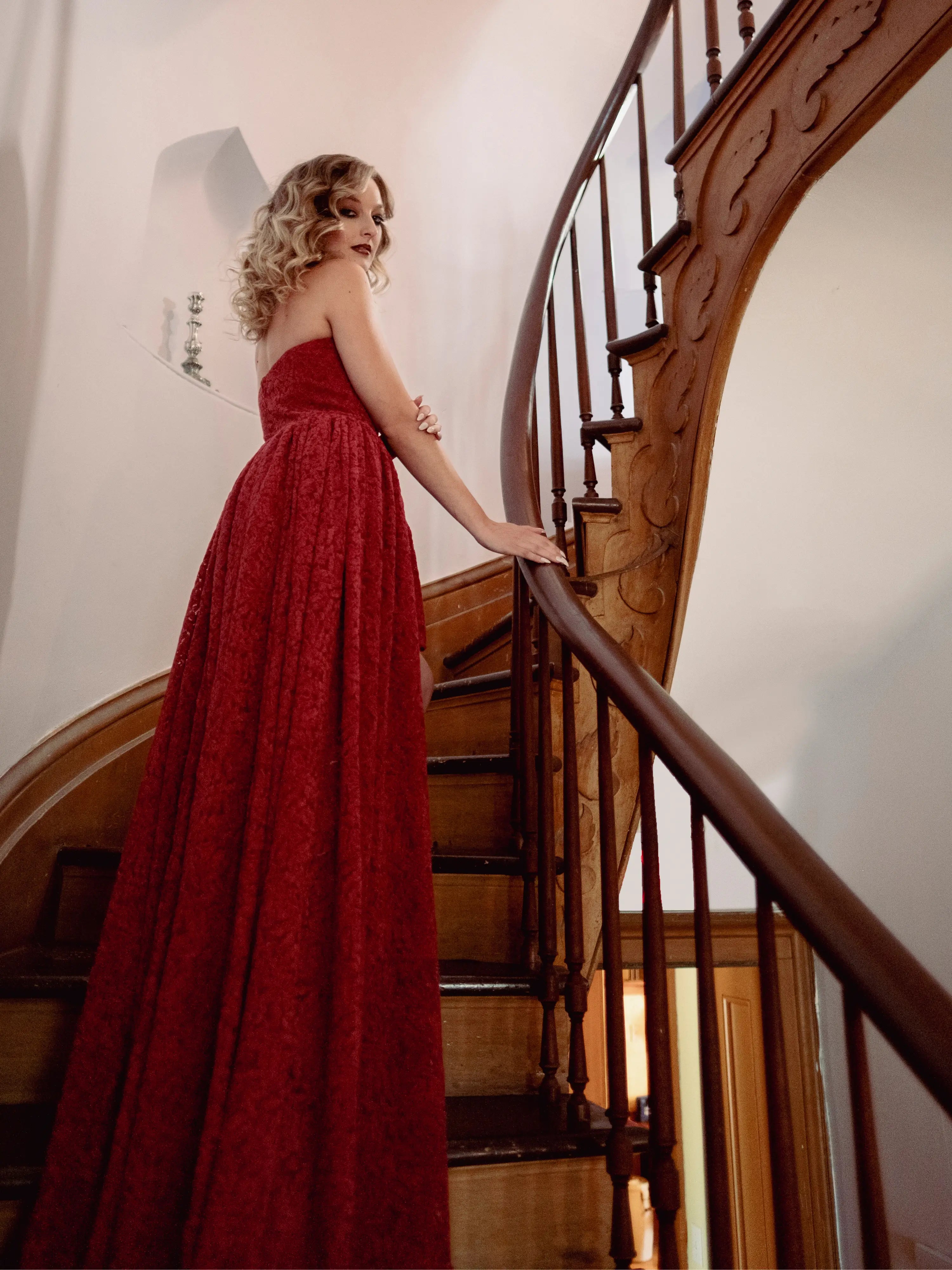 A woman in a red lace dress standing on a wooden staircase
