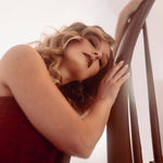 A woman in a red lace dress leaning against a wooden railing with a blurred background