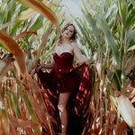 A woman wearing the Crimson Cathedral Dress standing in a cornfield