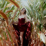 A woman wearing the Crimson Cathedral Dress standing in a cornfield