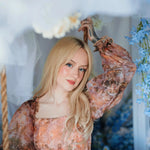 Portrait of a woman wearing a long sleeve ball gown highlighting the soft baroque print in a floral setting.