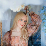 Portrait of a woman wearing a long sleeve ball gown highlighting the soft baroque print in a floral setting.