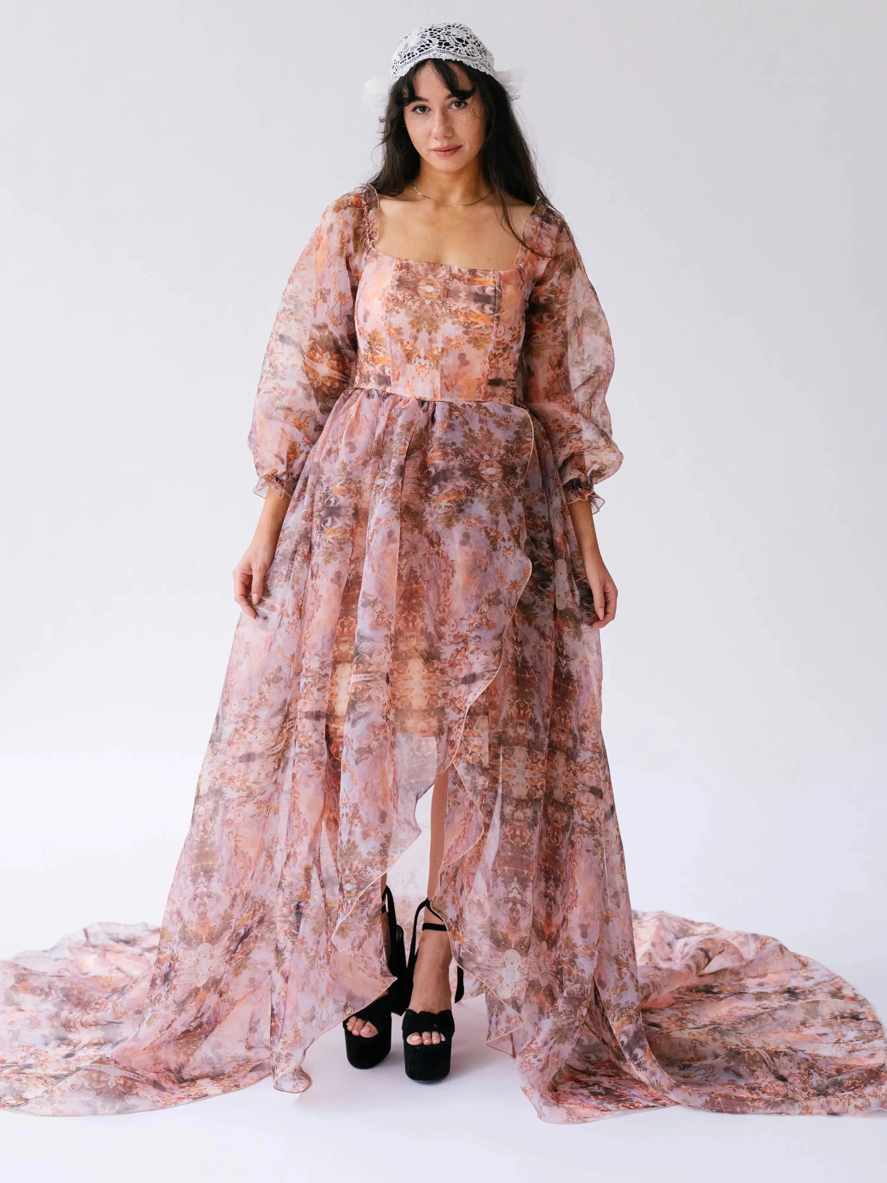 Model in a long sleeve ball gown showcasing the bishop sleeves and high-low slit, styled with black platform heels and tiara.