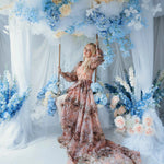 The Ode to Jove Twilight Reverie Ball Gown styled on a swing with trailing organza and floral backdrop, evoking a fairytale garden scene.