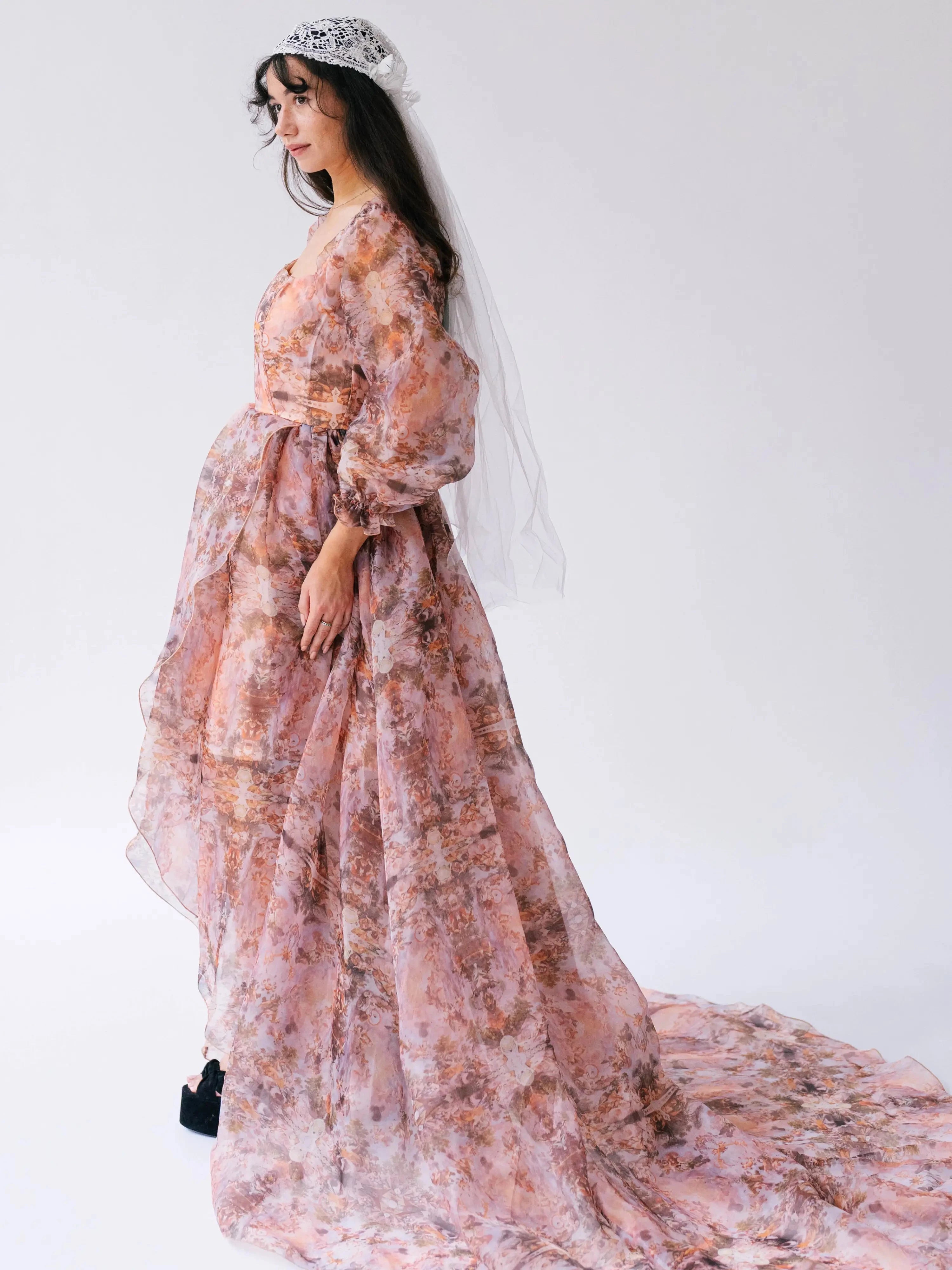 Side profile a woman wearing the Ode to Jove Twilight Reverie Ball Gown with long sleeves and flowing silhouette, styled with a tiara and veil.