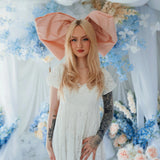 The Baby Antoinette Silk Hair Bow worn with a white lace dress, set against pastel floral decor for a coquette-inspired fashion look.