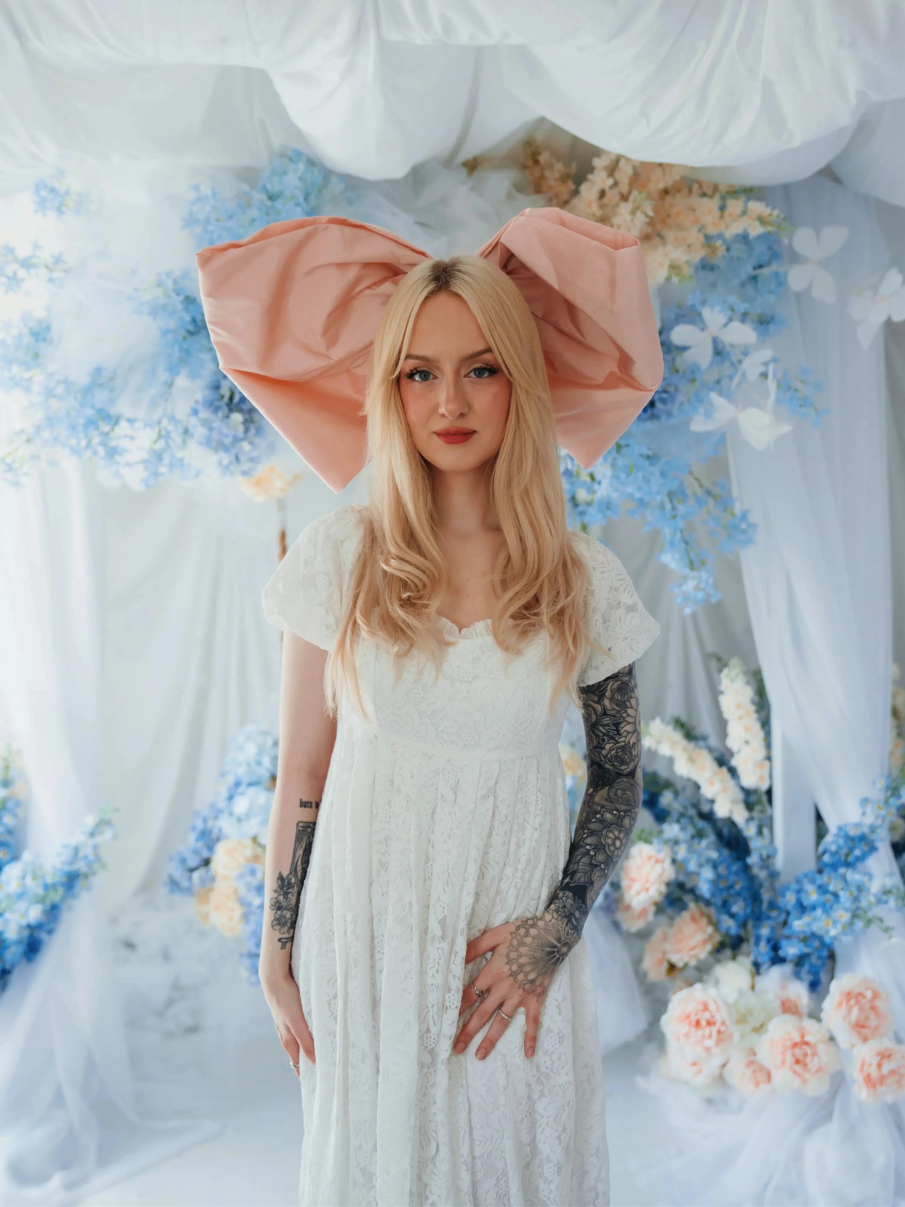 The Baby Antoinette Silk Hair Bow worn with a white lace dress, set against pastel floral decor for a coquette-inspired fashion look.